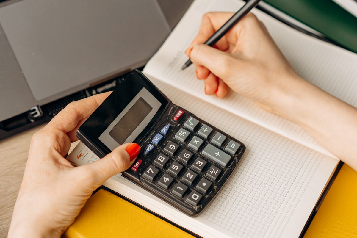 A person checking figures on a calculator and noting them in a lined notebook.